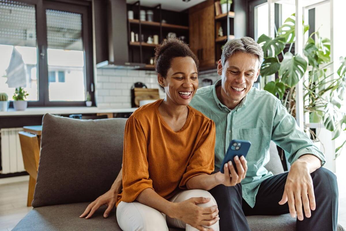 man and woman at home smiling and looking at phone together