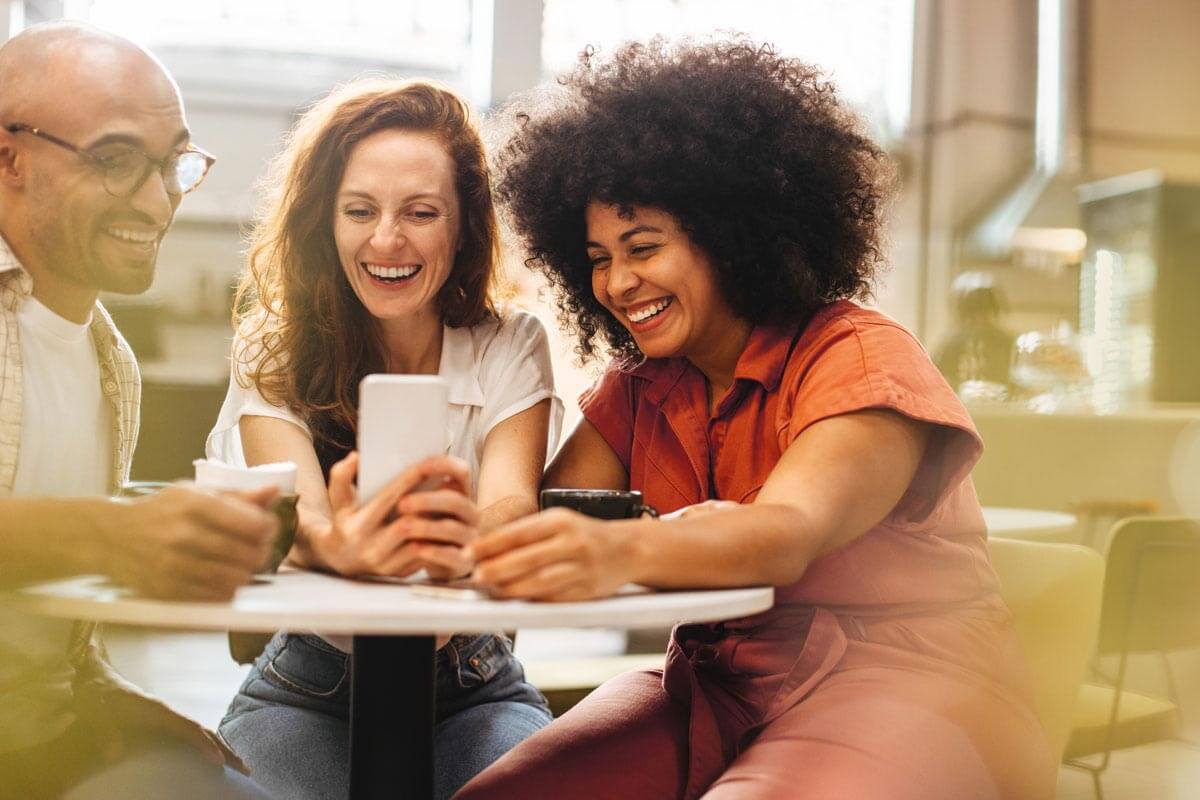 group of friends smiling and looking at phone together at cafe