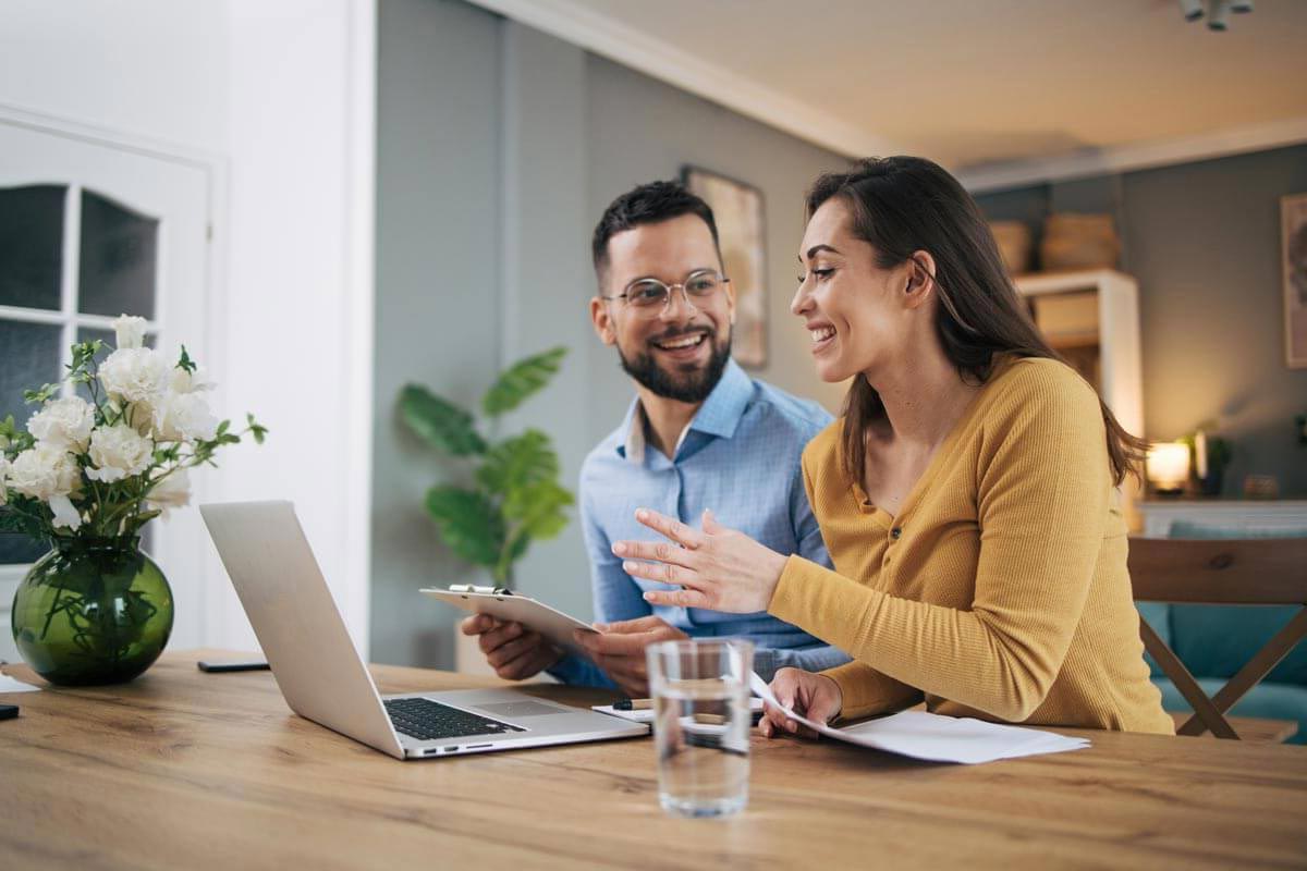 man with clipboard smiling and helping woman with laptop