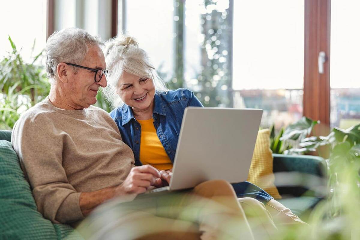 senior couple smiling on couch together looking at laptop