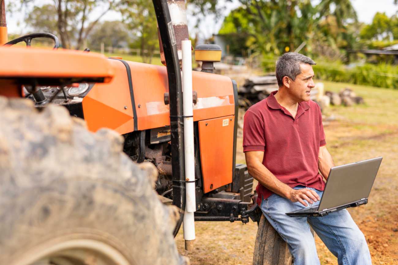 Person using a laptop beside a tractor on farmland with Internet Services, East Central Indiana